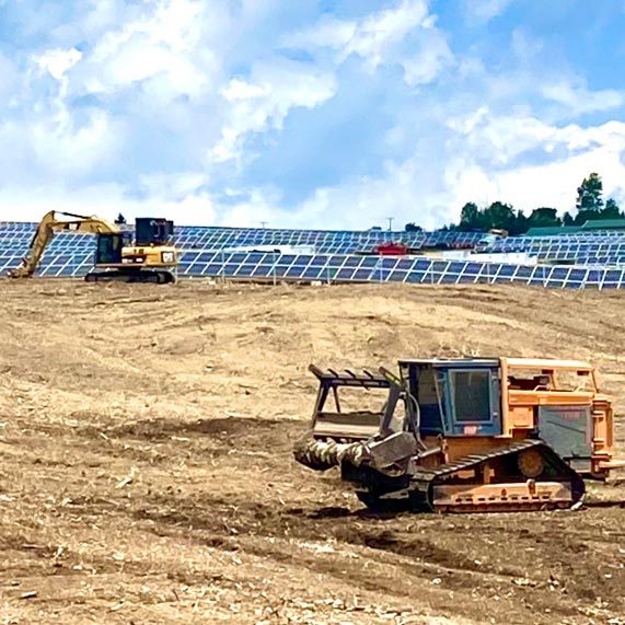A wide cleared site with an excavator and other machines moving soil and graded dirt