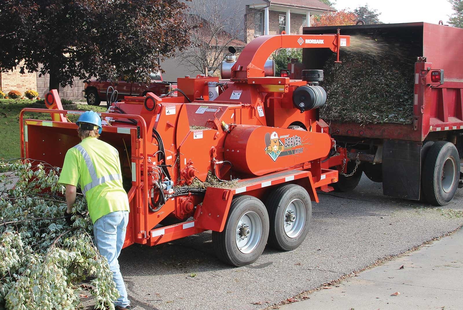 A worker in hi-vis gear feeding branches into a red wood chipper on a job site