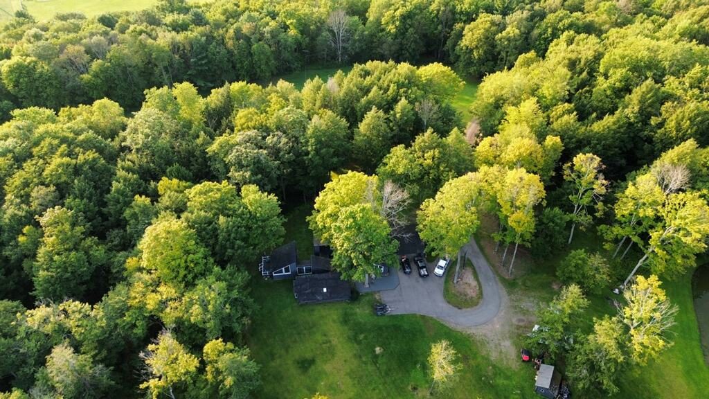 An aerial view of a house among the woods with its driveway